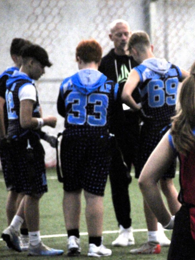 Fife All Stars flag football players in a huddle, listening to the coach.
